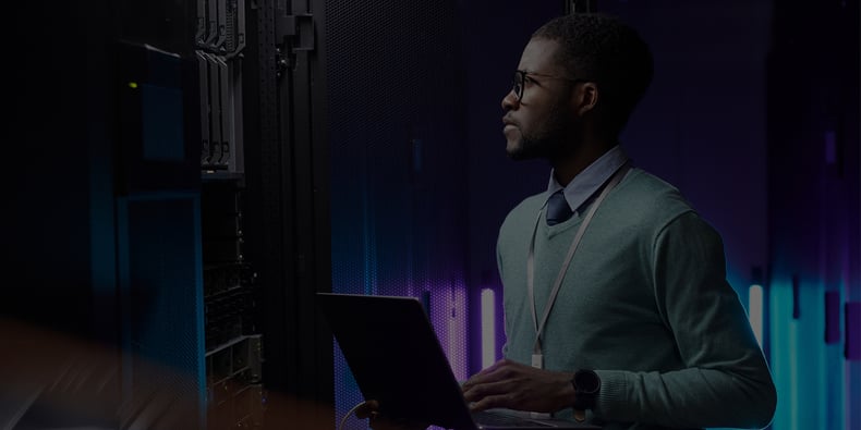 An IT professional wonders how to audit IT infrastructure; they hold a laptop computer. 